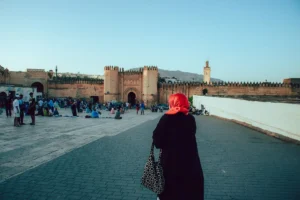 Woman in a red scarf walks towards an ancient city.